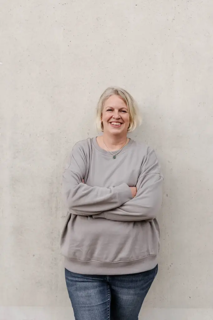 Antje Schwirz lehnt an einer grauen Betonwand, verschränkte Arme und schaut in die Kamera